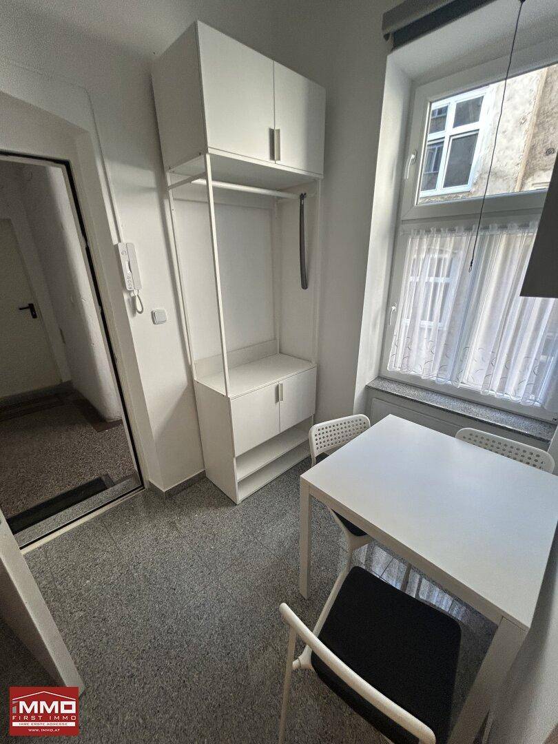 Heller Essbereich mit weißem Tisch und Stühlen, ergänzt durch eine offene Garderobe am Eingang.