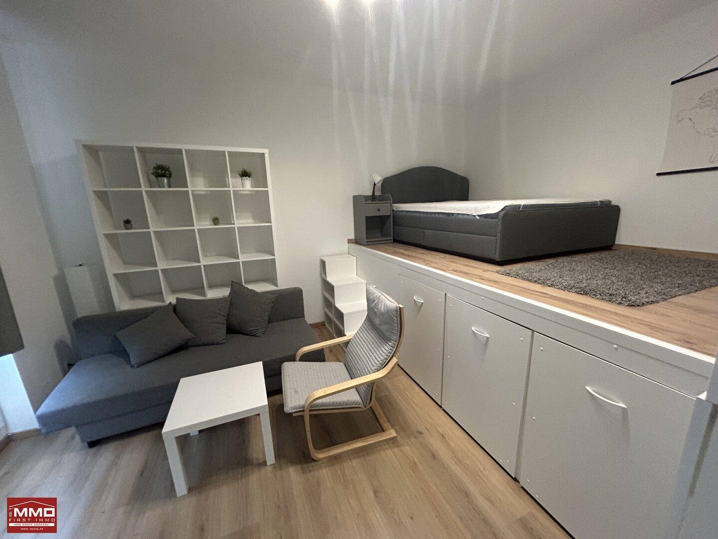 Gemütlicher Wohn- und Schlafbereich mit erhöhtem Bett auf einer praktischen Stauraumplattform.
