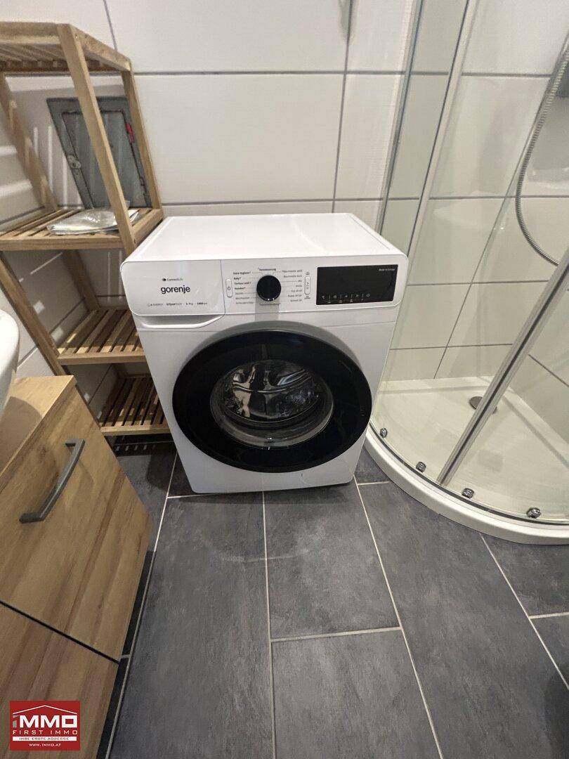 Nahaufnahme einer modernen Waschmaschine im Badezimmer, neben einem Holzregal.