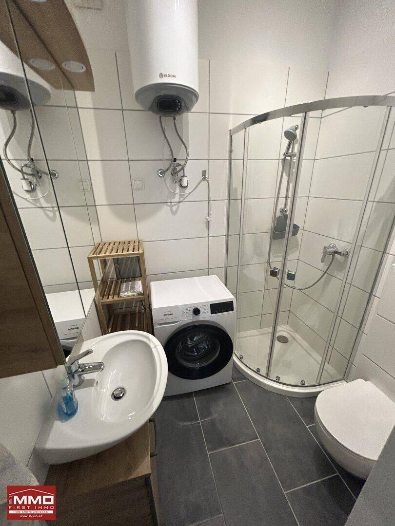 Komplettes Badezimmer mit Eckdusche, WC, Waschbecken und einer integrierten Waschmaschine.
