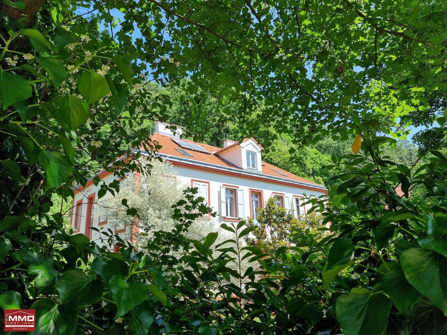 Charmantes Haus mit Satteldach und Dachgauben, umgeben von üppigem Grün unter blauem Himmel.
