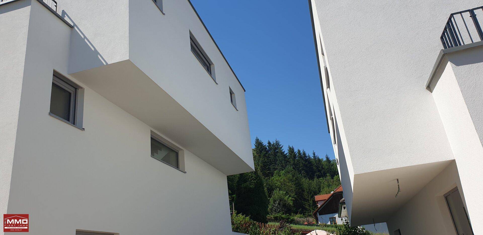 Moderne weiße Architektur mit klaren Linien unter blauem Himmel, umgeben von grünen Bäumen.