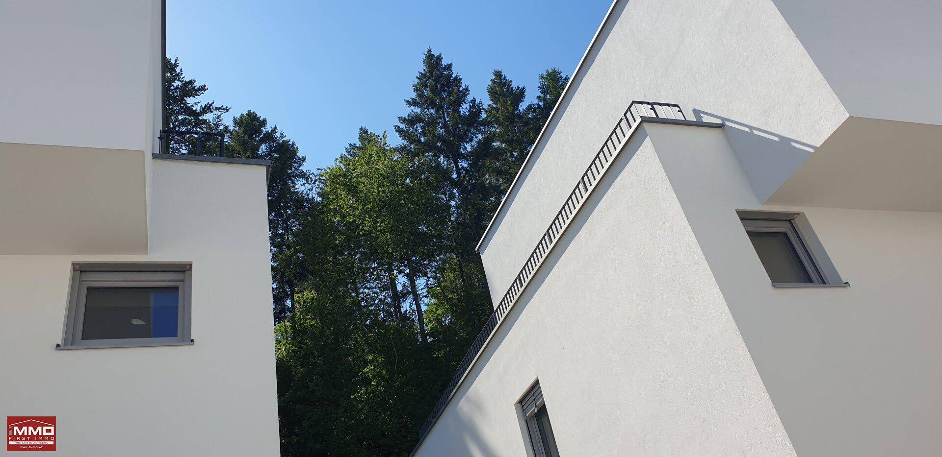 Geometrische Formen der modernen weißen Fassade im Kontrast zum blauen Himmel und den grünen Bäumen.