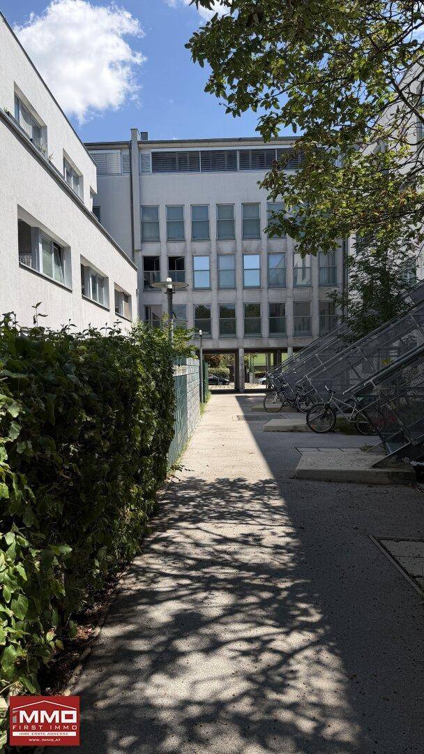 Moderner Gebäudekomplex mit gepflegten Außenanlagen, Wegen und Fahrradabstellplätzen unter blauem Himmel.