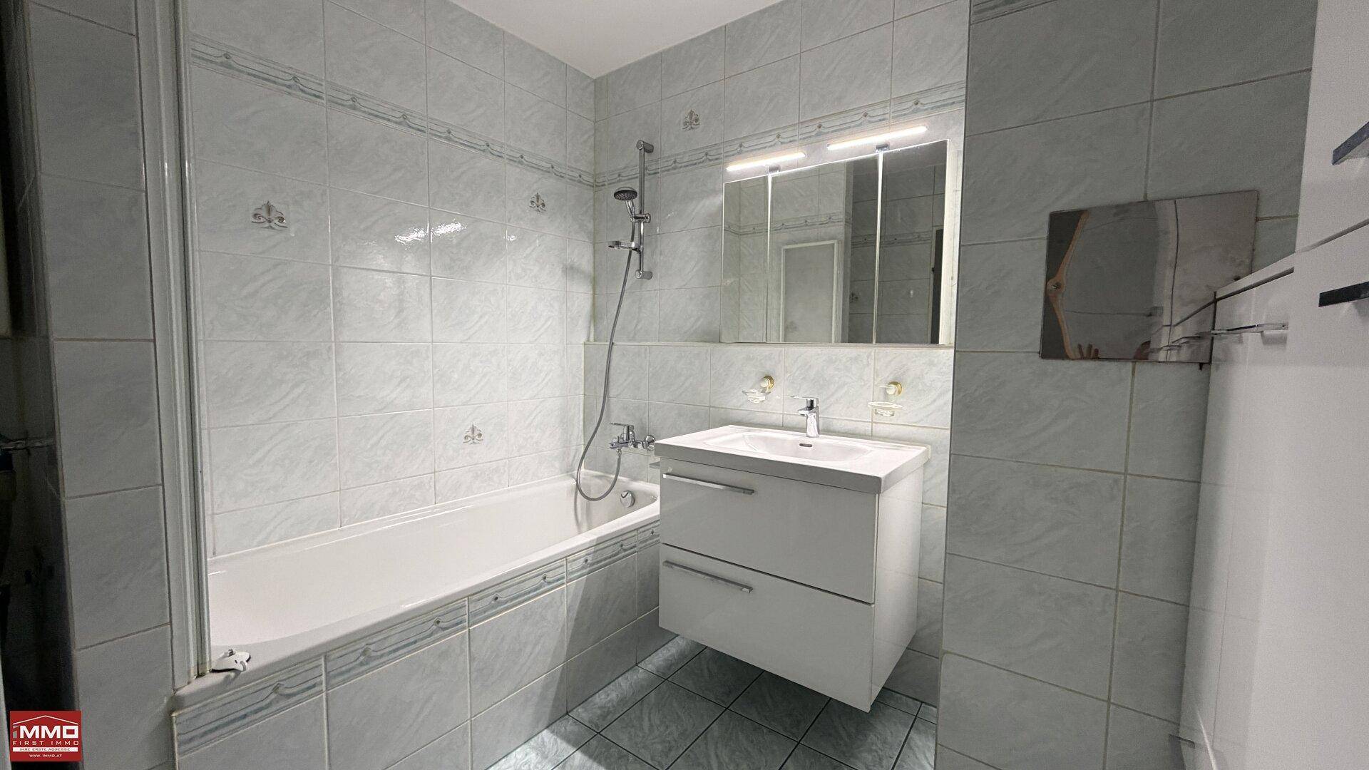 Funktionales Badezimmer mit Badewanne und modernem Waschtisch, ausgestattet mit hellen Fliesen.