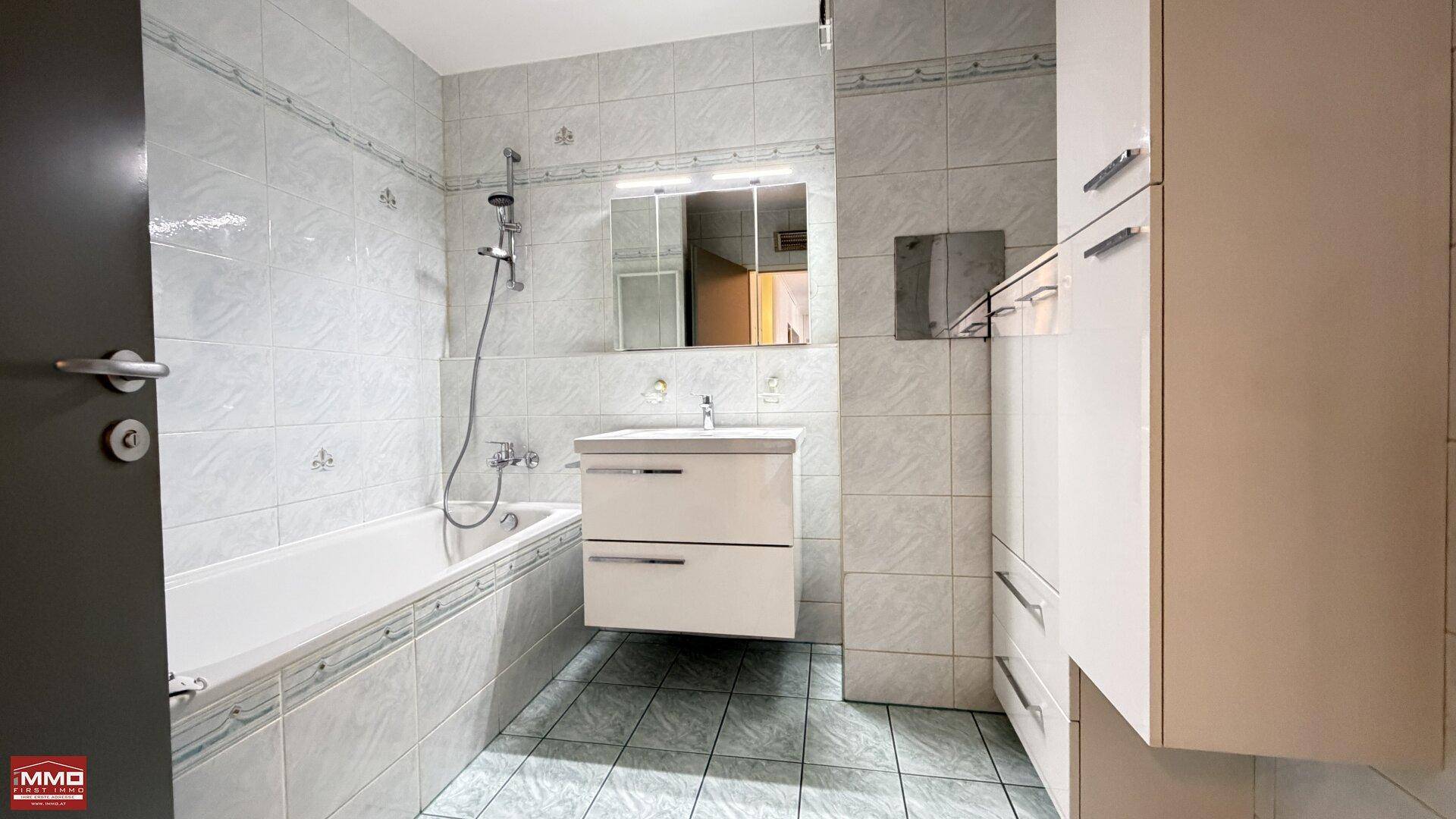 Helles Badezimmer mit Badewanne, Waschbecken und Spiegelschrank, komplett gefliest in hellen Tönen.