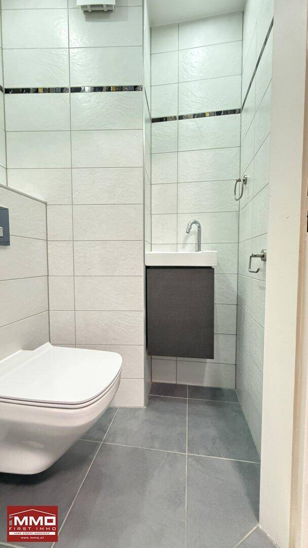 Modernes Gäste-WC mit wandhängender Toilette und kleinem Waschbecken, vollständig gefliest.