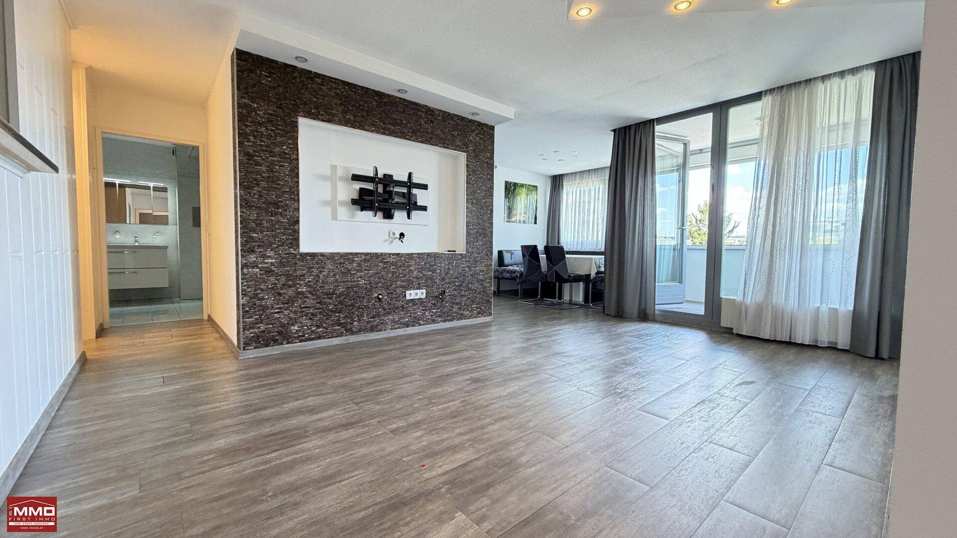 Großzügiges Wohnzimmer mit modernem Fliesenboden, Steinwand und Zugang zum Balkon.