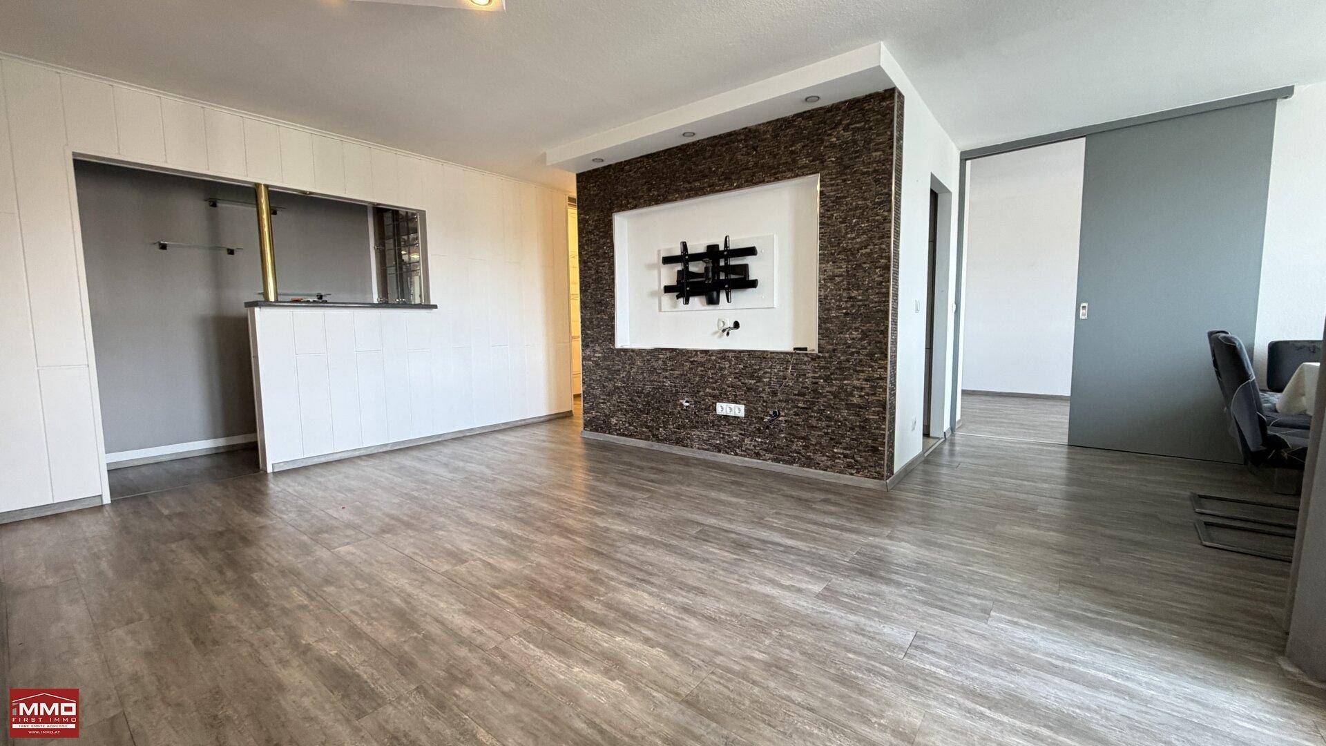Offener Wohnbereich mit dekorativer Steinwand, modernem Boden und Durchgang zur Küche.