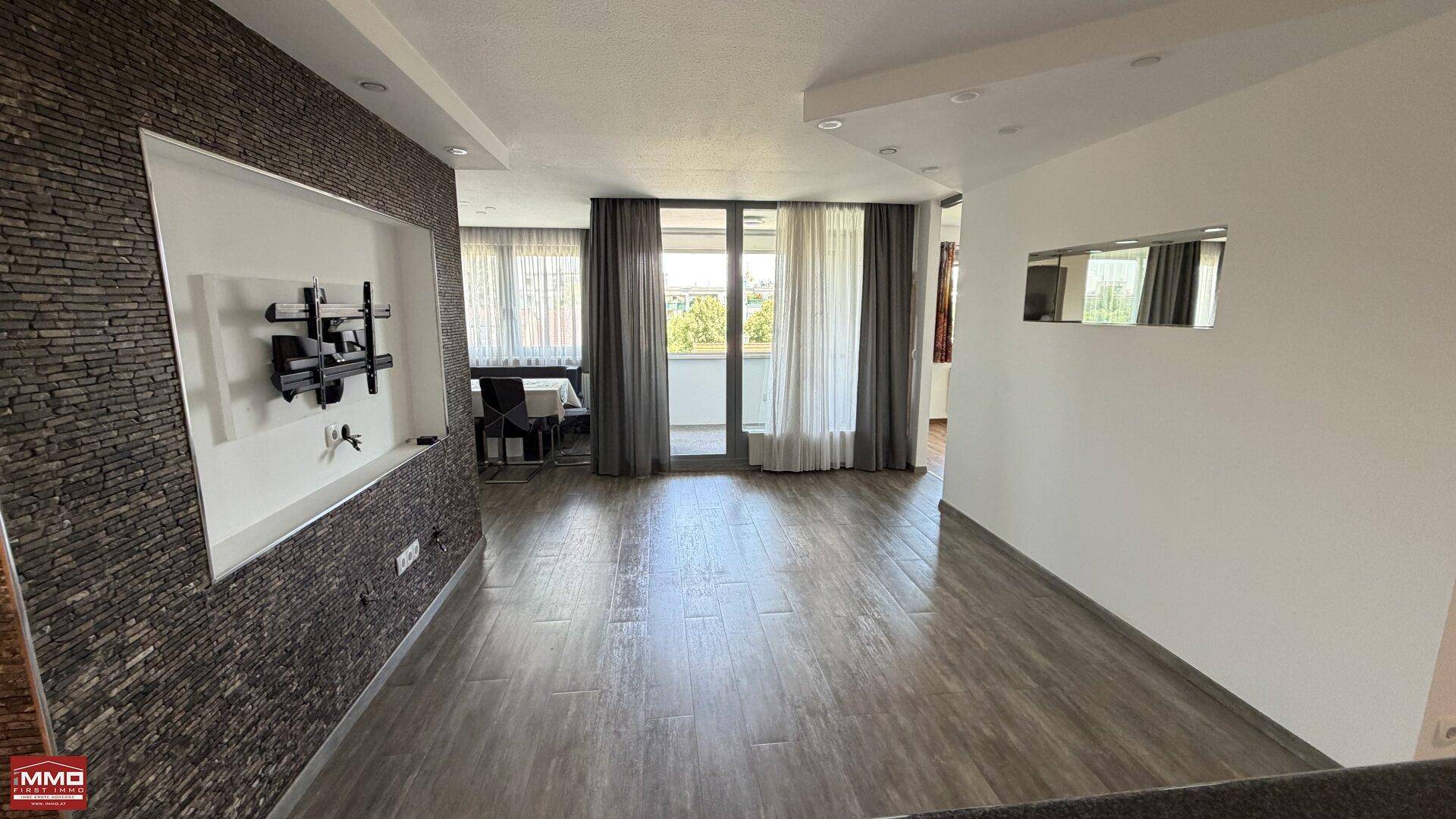 Helles Wohnzimmer mit stilvoller Steinwand, Fliesenboden und großen Fenstern zur Loggia.
