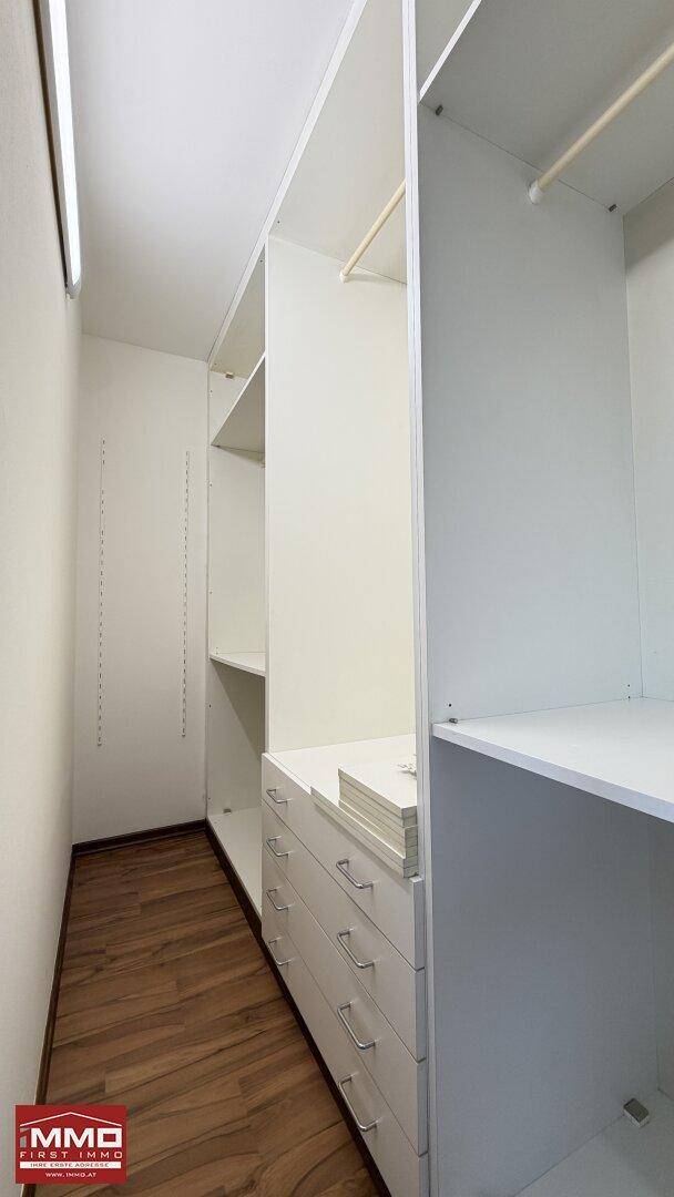 Praktischer begehbarer Kleiderschrank mit weißen Regalen und Schubladen für viel Stauraum.