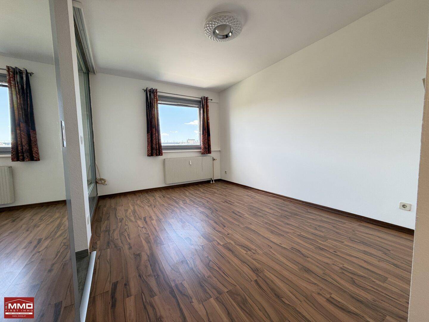 Helles Schlafzimmer mit Laminatboden, weißen Wänden und einem Fenster mit Ausblick.