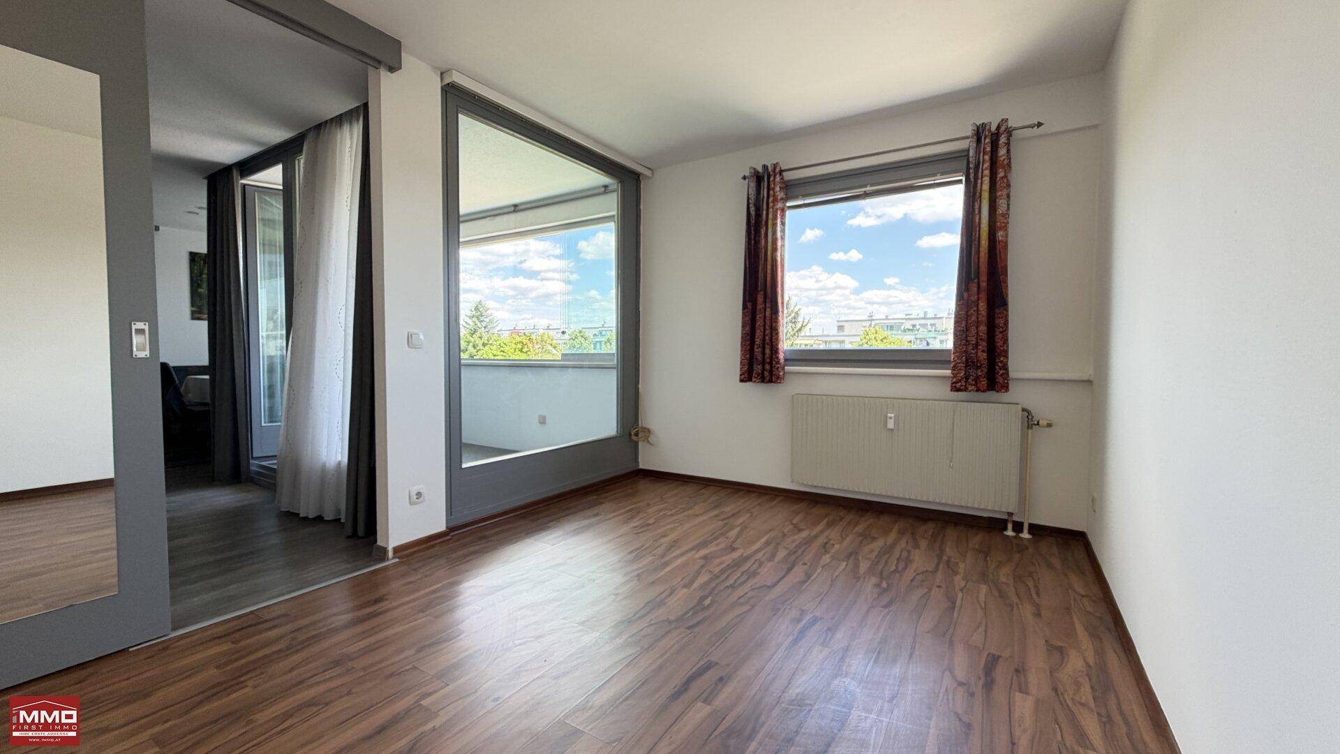 Schlafzimmer mit Laminatboden, hellen Wänden und direktem Zugang zur verglasten Loggia.