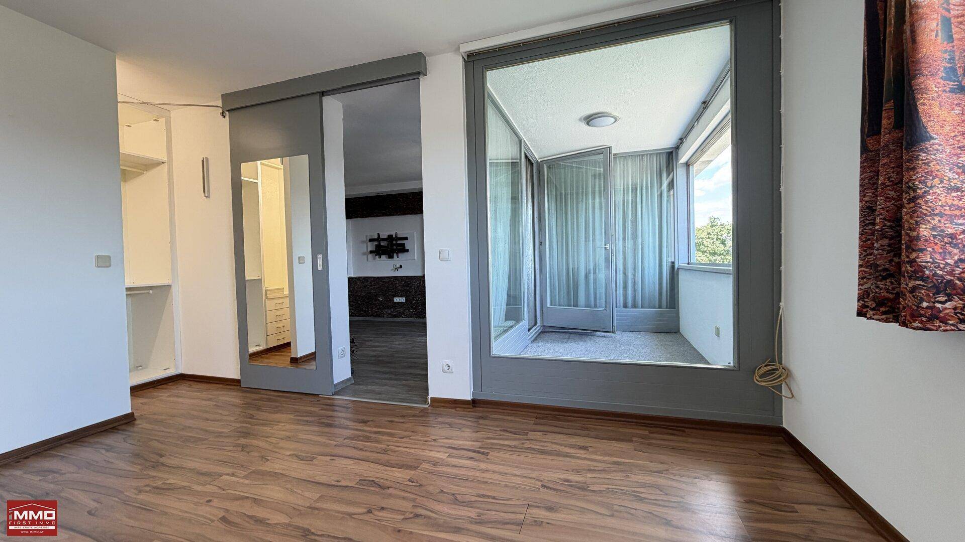 Schlafzimmer mit Laminatboden, Schiebetür zum Ankleidezimmer und Zugang zur Loggia.