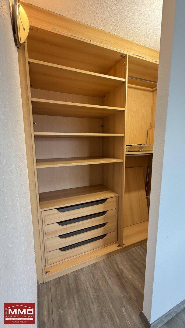 Geräumiger begehbarer Kleiderschrank mit Holzregalen und Schubladen für optimale Organisation.
