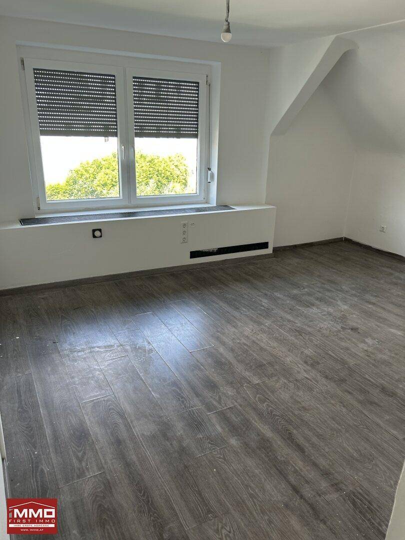 Helles Zimmer mit Laminatboden und großem Fenster, bereit zur individuellen Einrichtung.