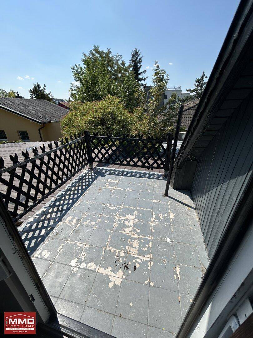 Kleiner Balkon mit Gittergeländer und Blick auf die umliegenden Häuser und Bäume.