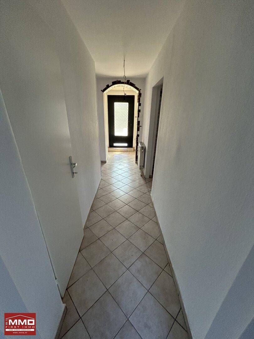 Langer Flur mit Fliesenboden und weiß gestrichenen Wänden, verbindet die Zimmer.