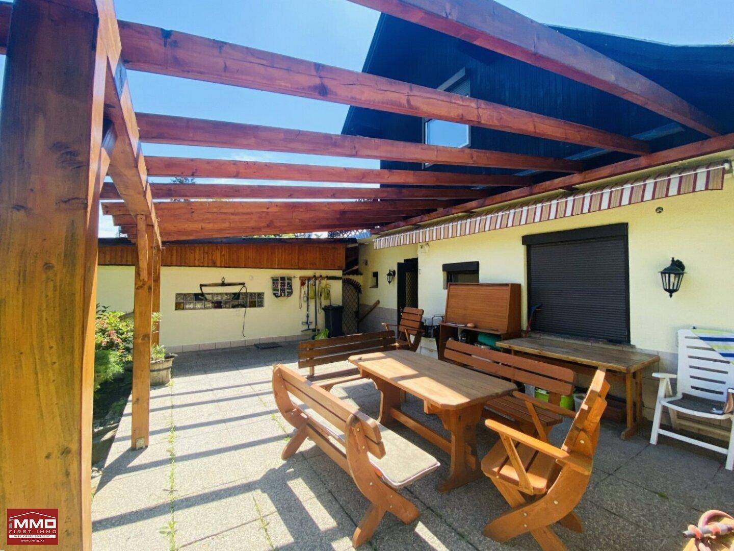 Detailansicht der Terrasse mit rustikalen Holzmöbeln und einer schattenspendenden Holzpergola.