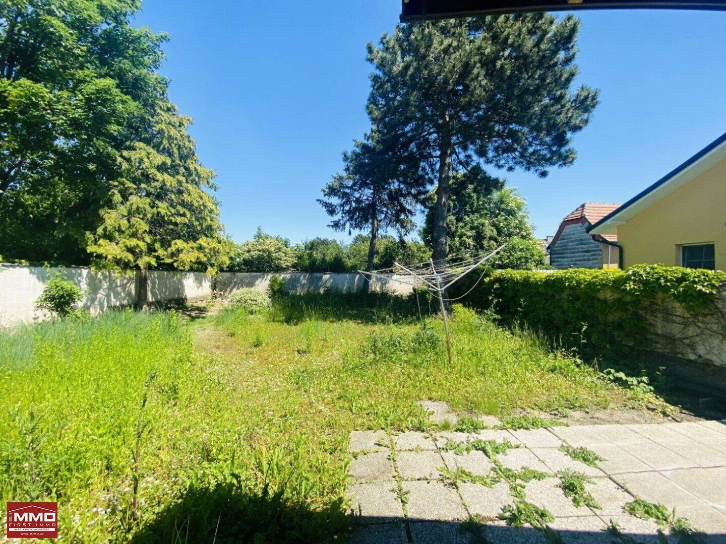 Weitläufiger Garten mit Rasenfläche und umgebenden Mauern unter strahlend blauem Himmel.