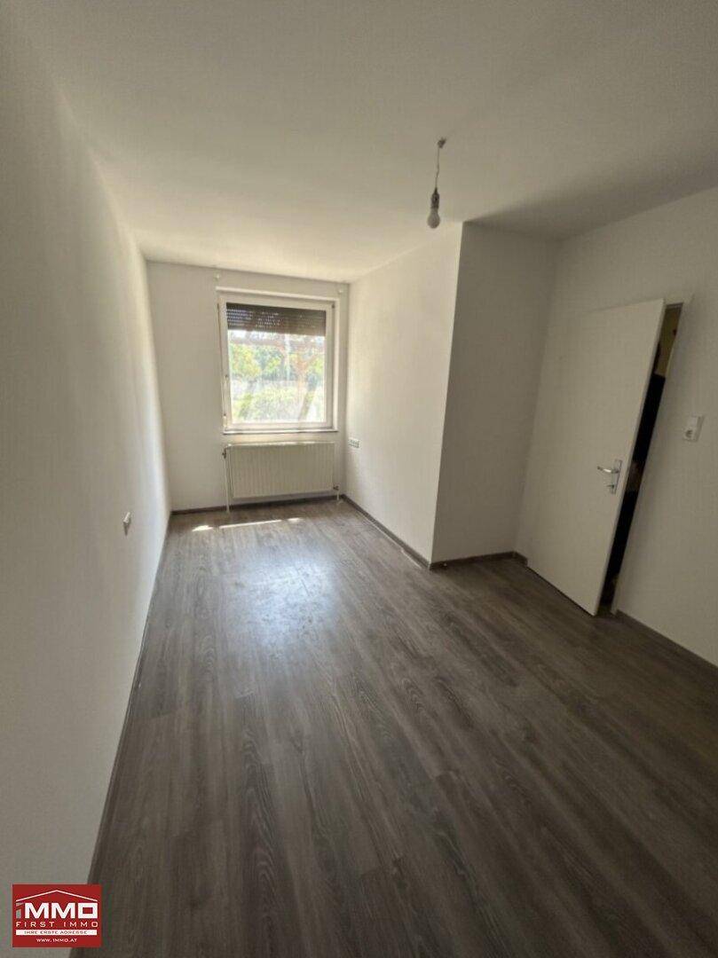 Helles Schlafzimmer mit modernem Laminatboden und Fenster mit Blick ins Grüne.