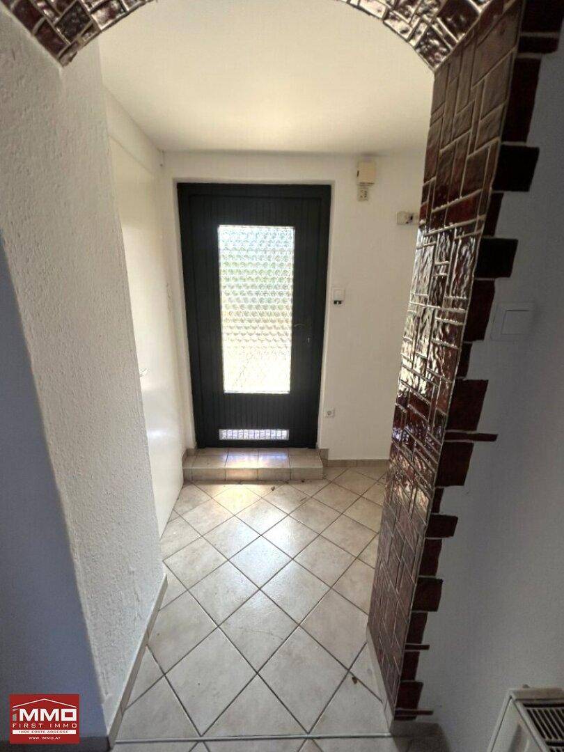 Eingangsbereich mit Fliesenboden und einer dekorativen Kachelwand, die zum Wohnbereich führt.