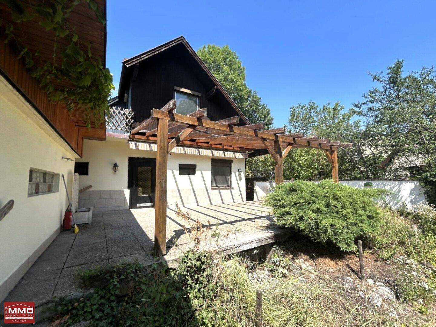 Seitlicher Zugang zum Haus und die großzügige Terrasse mit Holzpergola und viel Sonnenlicht.