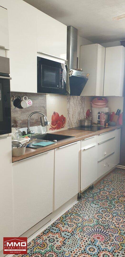 Moderne Küche mit weißen Schränken, Holzarbeitsplatte und farbenfrohem gemustertem Fliesenboden.