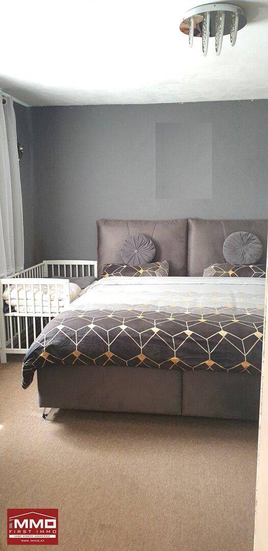 Schlafzimmer mit großem Doppelbett, Babybett und grauen Wänden, ausgestattet mit Teppichboden.