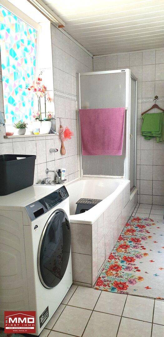 Badezimmer mit Badewanne, Duschkabine und Waschmaschine, ausgestattet mit hellen Fliesen.
