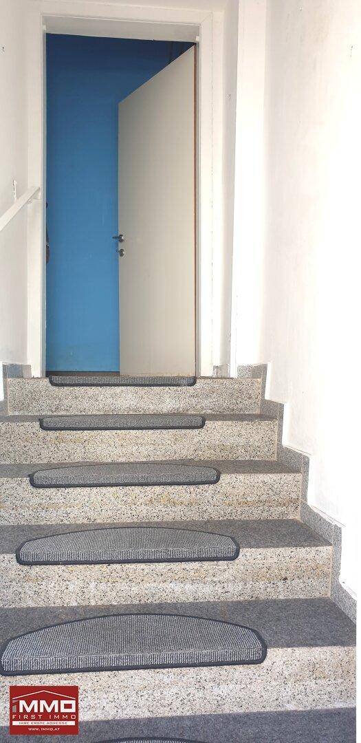 Treppenhaus mit Steinstufen und Teppichläufern, das zu einem oberen Stockwerk führt.