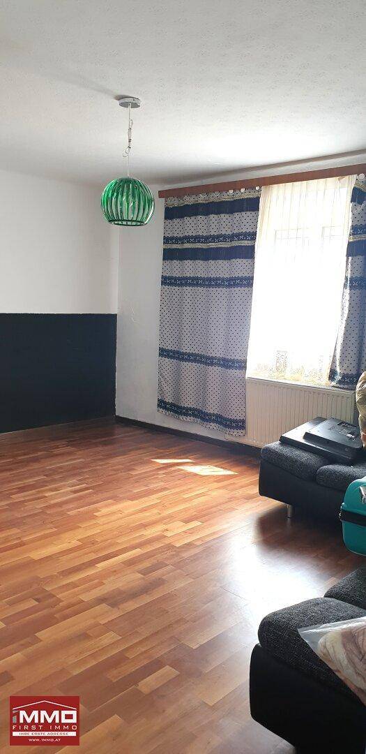 Wohnzimmer mit Holzboden, Fenster und einem grünen Deckenlicht, die Wände sind zweifarbig.