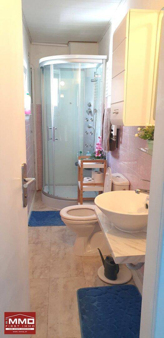 Schlichtes Badezimmer mit Duschkabine, Toilette und Waschbecken, ausgestattet mit rosa Fliesen.