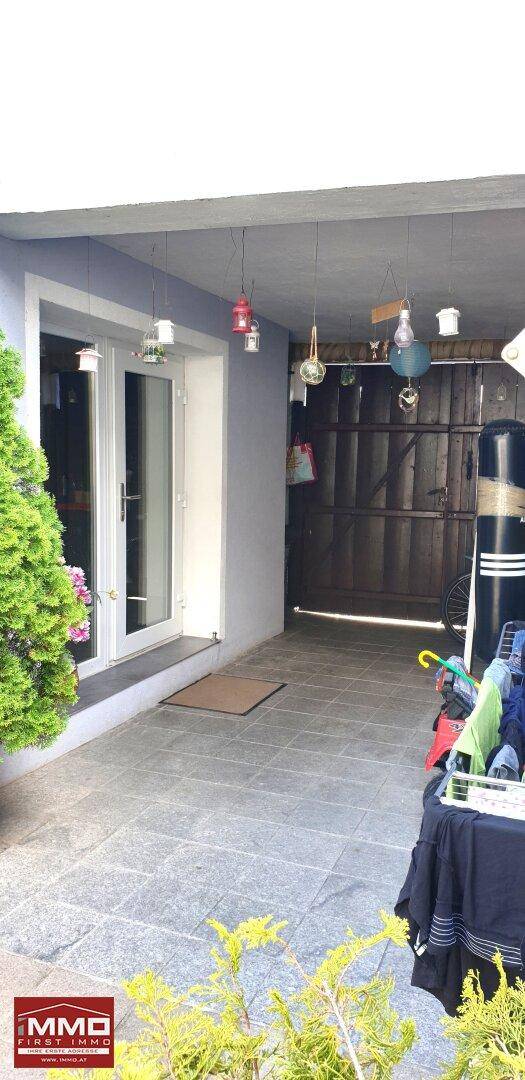 Überdachter Außenbereich mit gepflastertem Boden und Blick auf einen Garagenbereich.