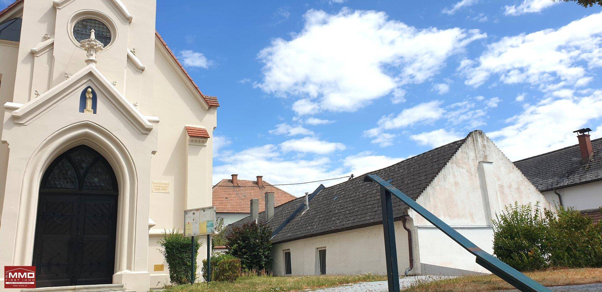 Historische Kirche mit Spitzbogenfenstern und einem angrenzenden Wohnhaus unter blauem Himmel.