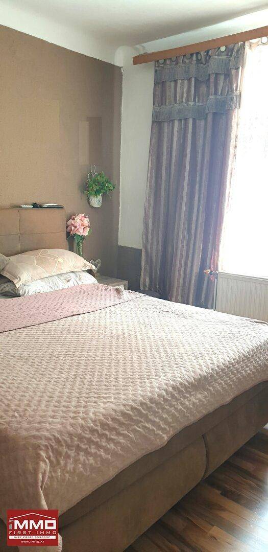 Helles Schlafzimmer mit Holzboden, großem Bett und Vorhängen am Fenster.