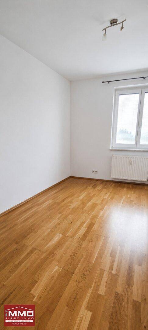 Helles Zimmer mit Parkettboden und einem Fenster, das für angenehme natürliche Belichtung sorgt.