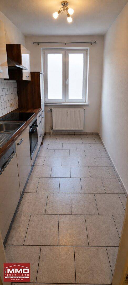 Funktionale Küche mit Fliesenboden, Einbauschränken und einem Fenster für natürliche Helligkeit.
