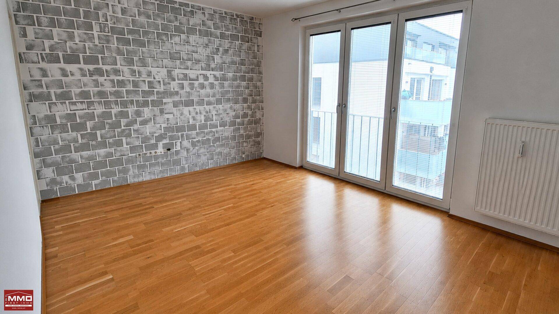 Geräumiges Zimmer mit Parkettboden, einer dekorativen Ziegelwand und Balkonzugang.