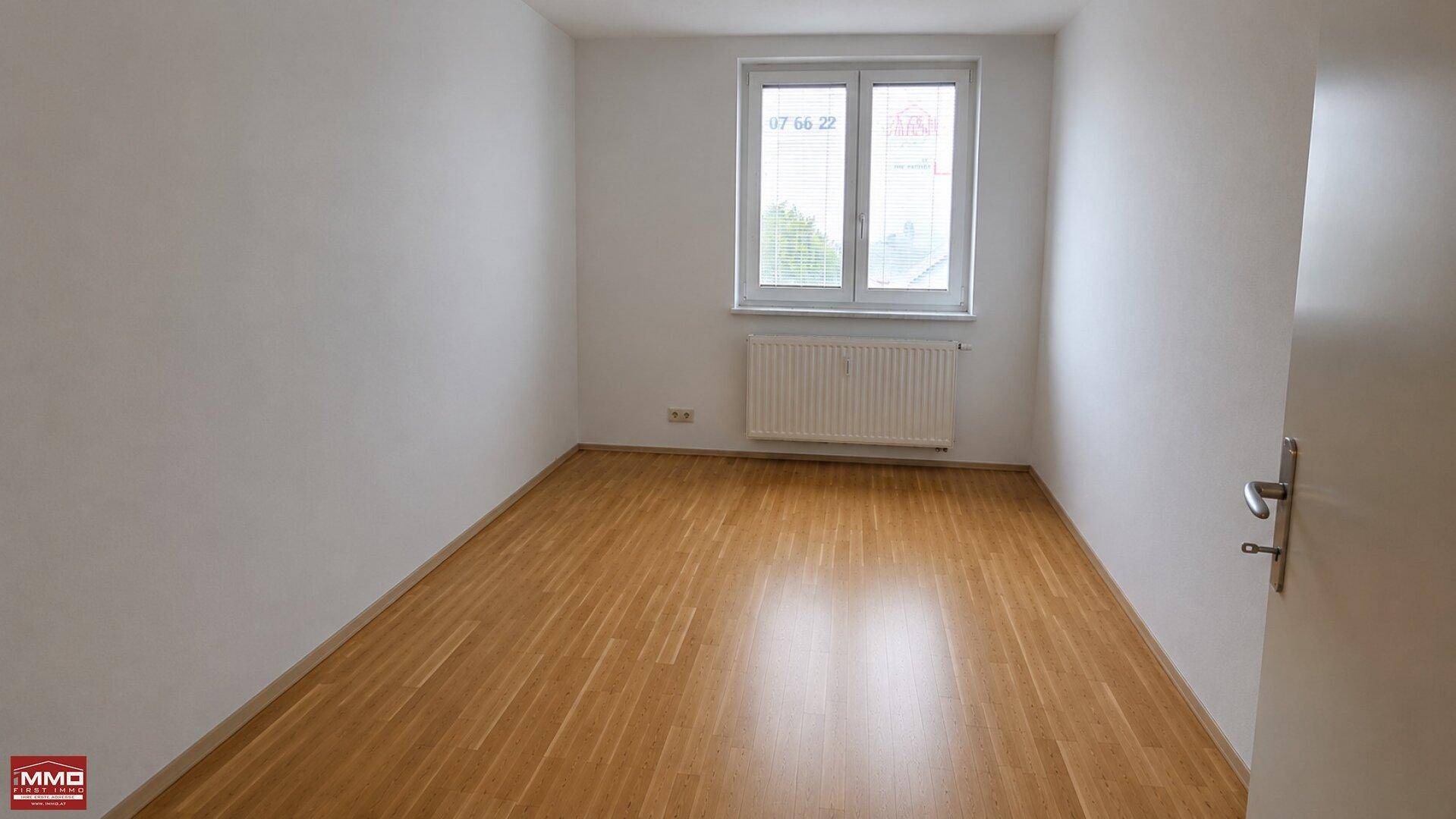 Leeres Zimmer mit Parkettboden und einem Fenster, das den Raum mit Tageslicht füllt.