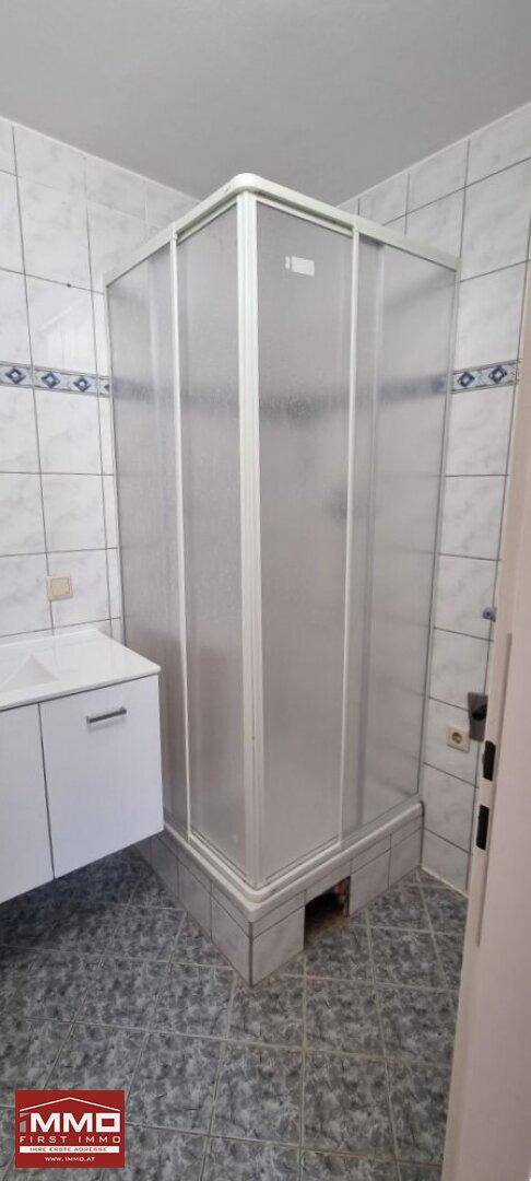 Funktionale Duschkabine im gefliesten Badezimmer, umgeben von hellen Wand- und Bodenfliesen.