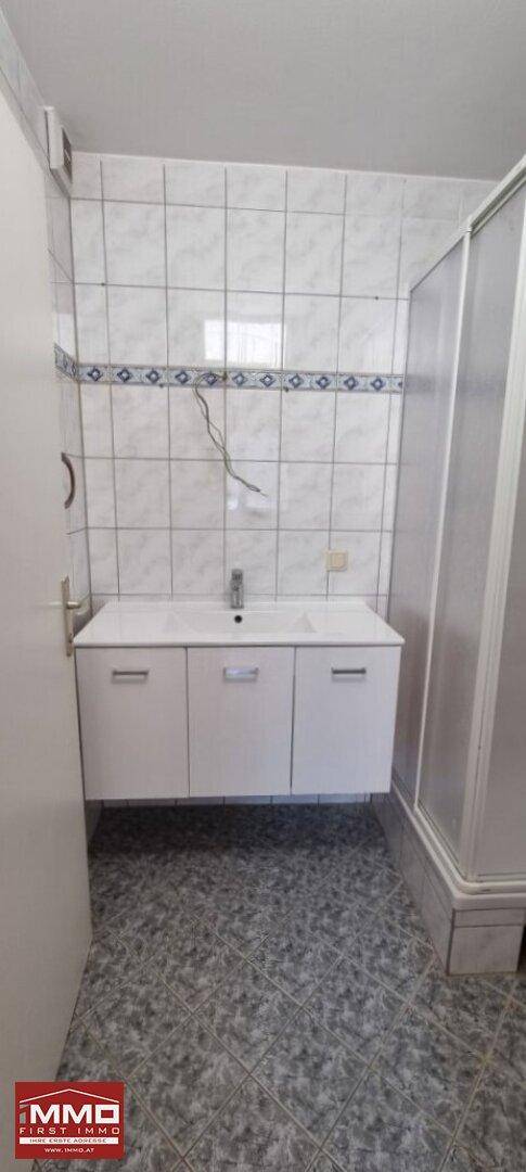 Badezimmer mit modernem Waschbeckenunterschrank, Spiegel und einer praktischen Duschkabine.