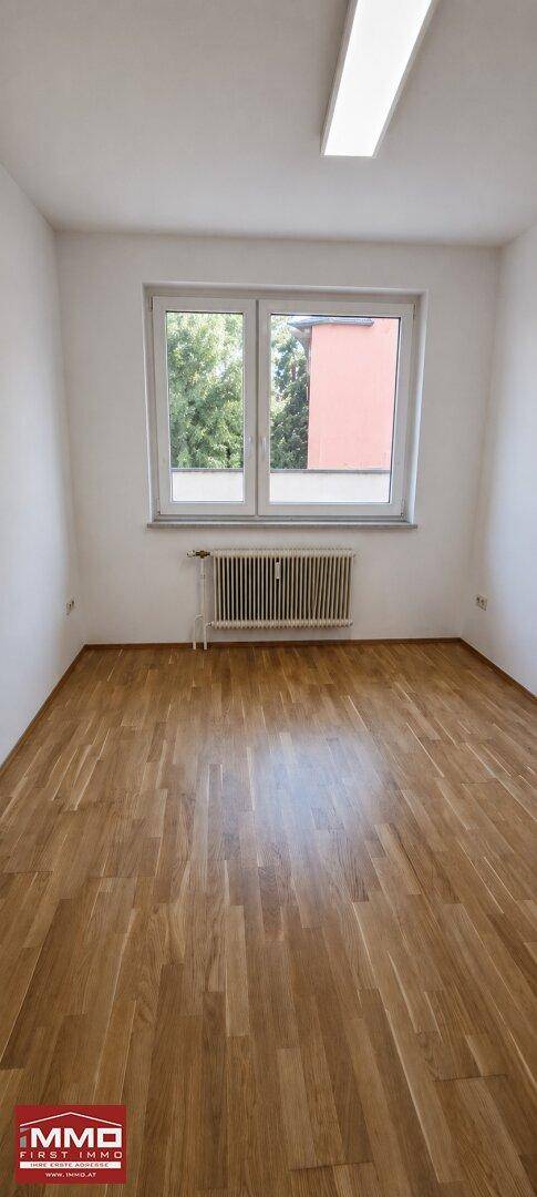 Heller Raum mit Parkettboden und einem Fenster, das den Blick ins Grüne freigibt.