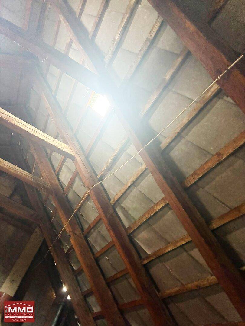 Heller Dachbodenbereich mit freiliegenden Holzbalken und natürlichem Lichteinfall durch ein Dachfenster.