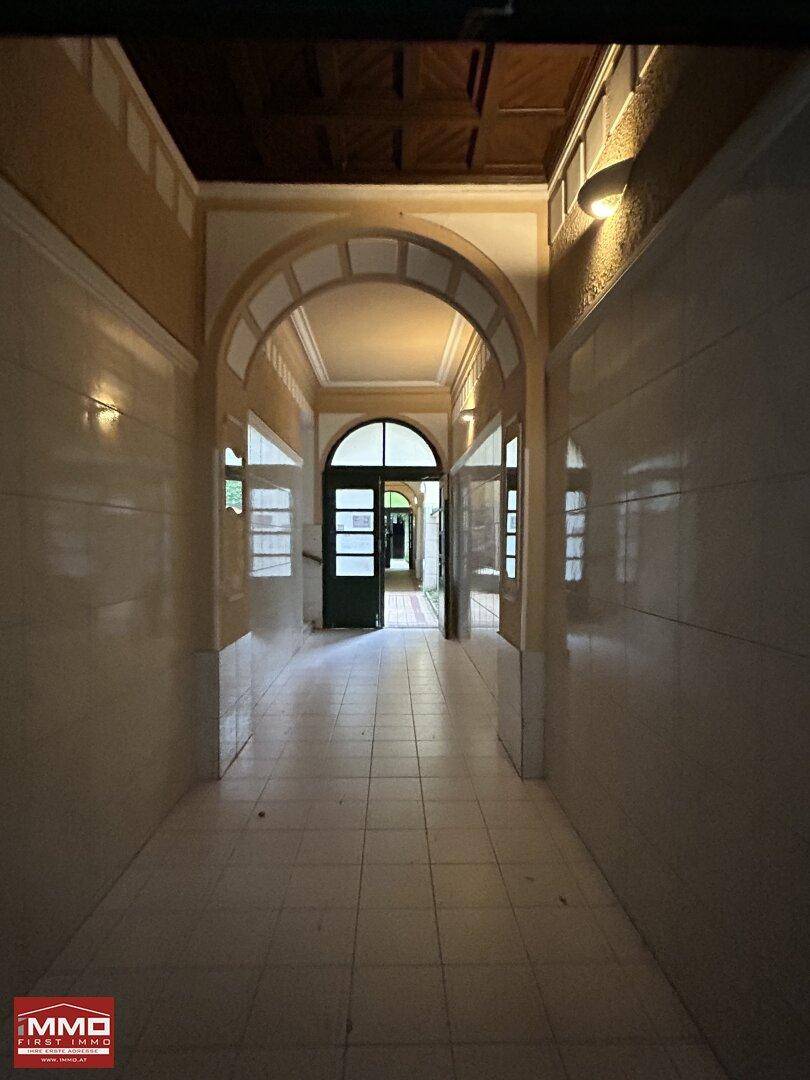 Langer, gefliester Flur eines Altbaus mit eleganten Bögen und Holztüren am Ende.