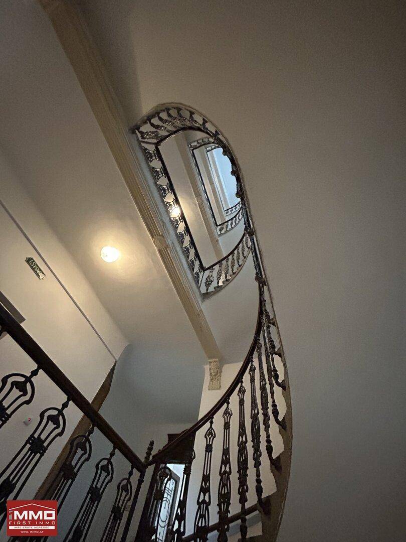 Elegantes Treppenhaus mit kunstvollen schmiedeeisernen Geländern und hohen Decken in einem Altbau.