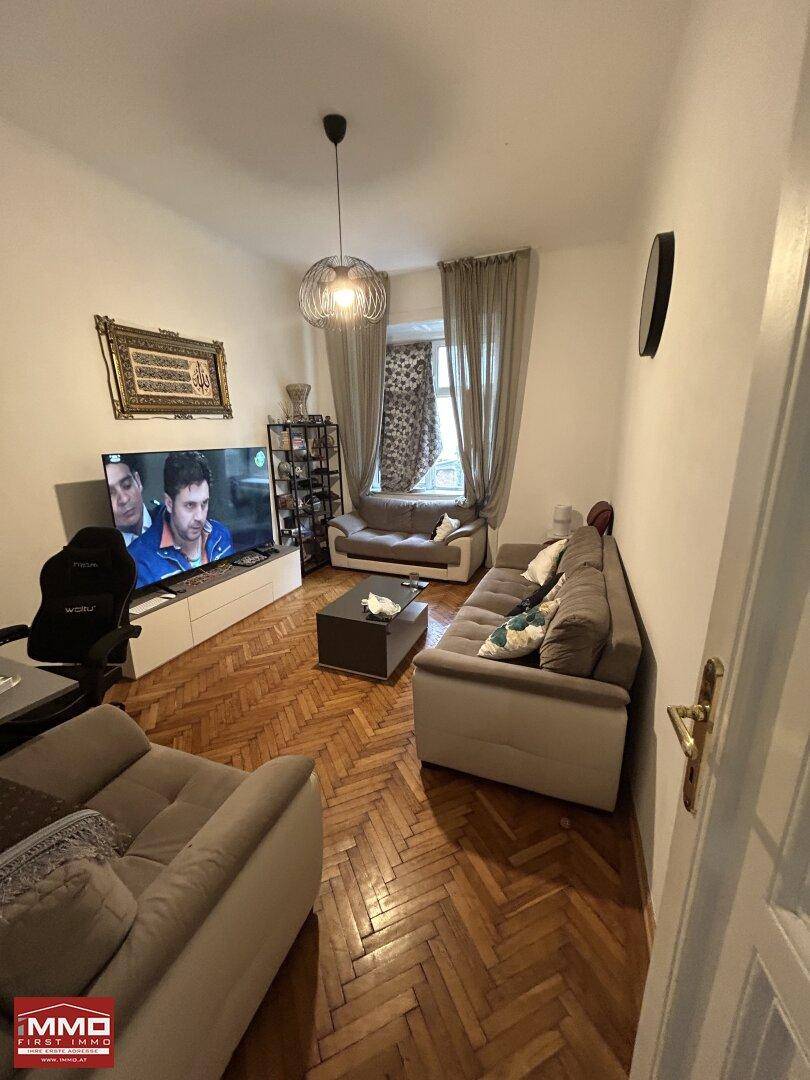 Gemütliches Wohnzimmer mit Fischgrätparkett, bequemen Sofas und einem Fernseher.
