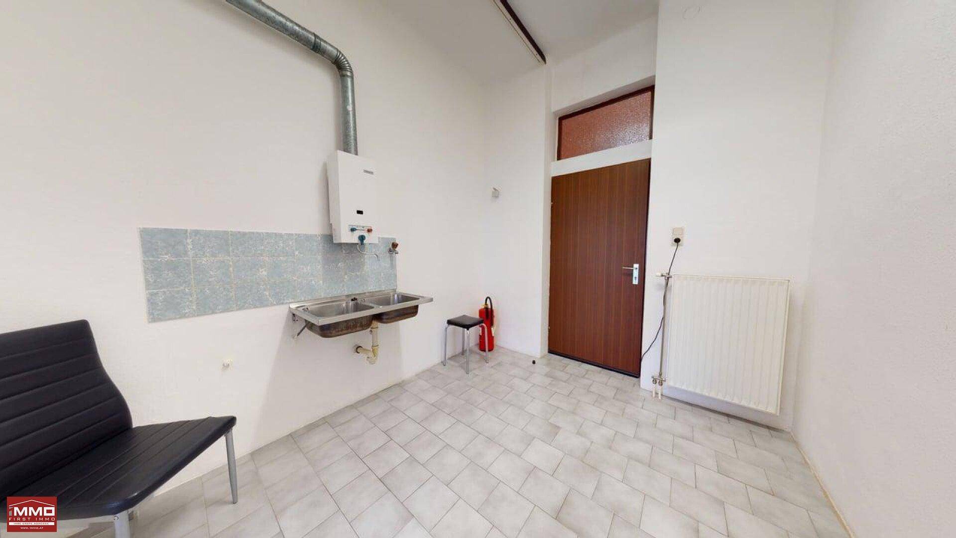 Einfacher Wirtschaftsraum mit Doppelspülbecken, Warmwasserbereiter und Fliesenboden, bereit zur Nutzung.