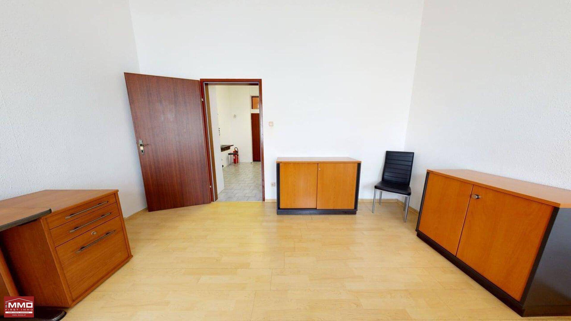 Büro mit hellem Laminatboden, zwei Holzschränken und einer offenen Tür, die zu einem weiteren Raum führt.