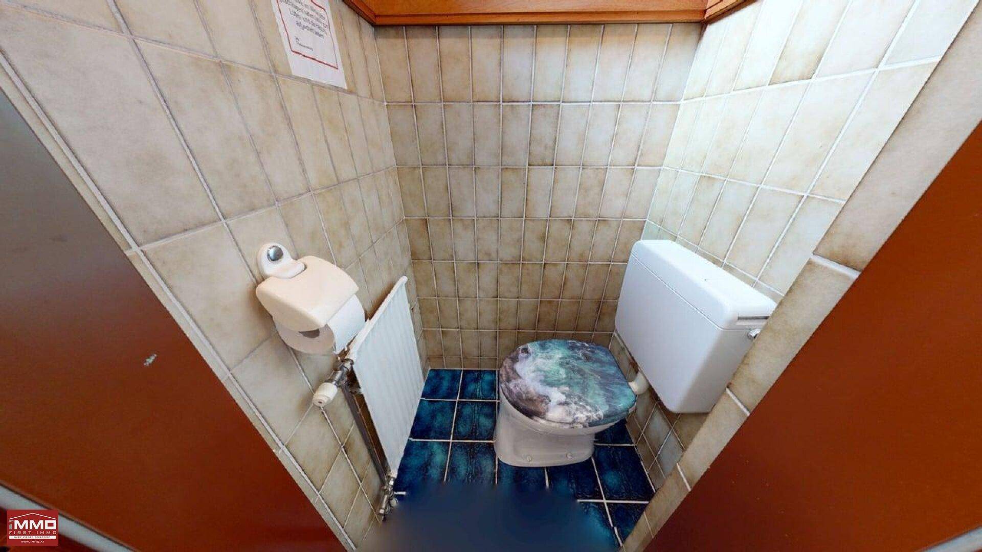 Kleiner Toilettenraum mit beigefarbenen Wandfliesen und blauen Bodenfliesen, ausgestattet mit einer Toilette.